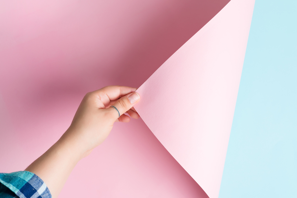 Hand, die rosa Papier gegen blauen Hintergrund anhebt