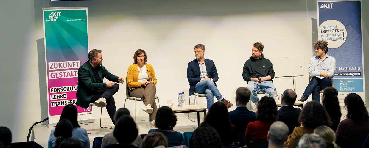 Podiumsdiskussion mit vier Personen und Publikum in einem modernen Konferenzraum.