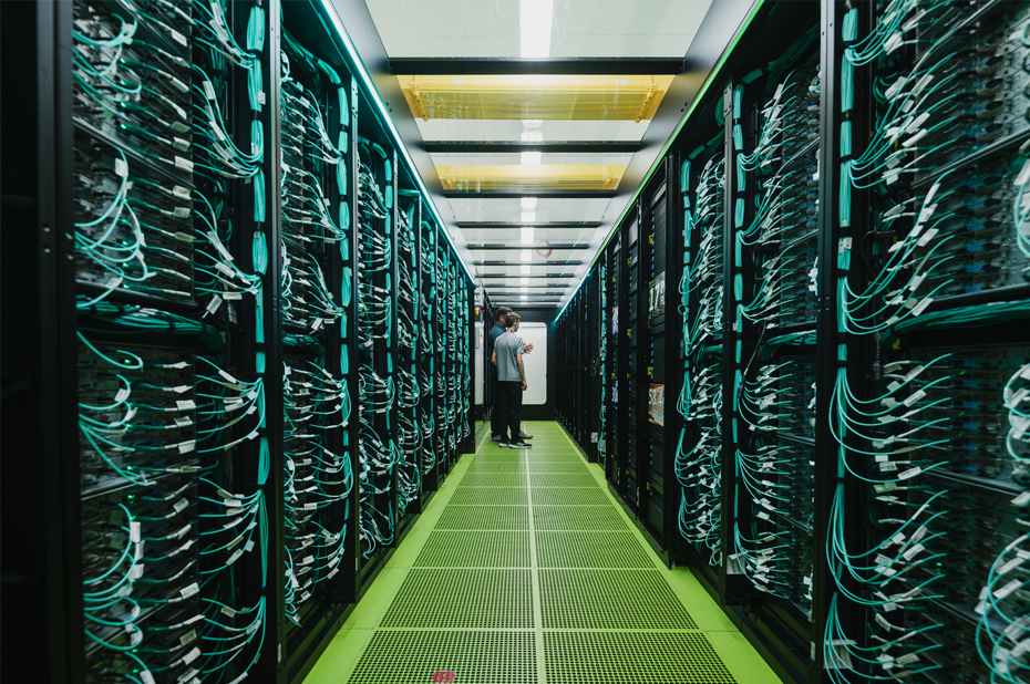 Rechenzentrum mit Serverracks und vielen Kabeln, zwei Techniker prüfen Verbindungen.